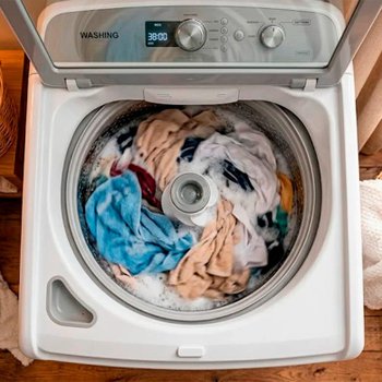 Máquina de lavar roupas aberta com peças coloridas e espuma, demonstrando uso do amaciante Comfort