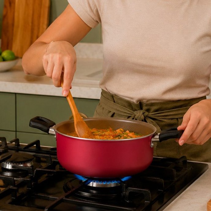 Mulher mexendo sopa de legumes com colher de pau em caçarola vermelha marca no fogão aceso
