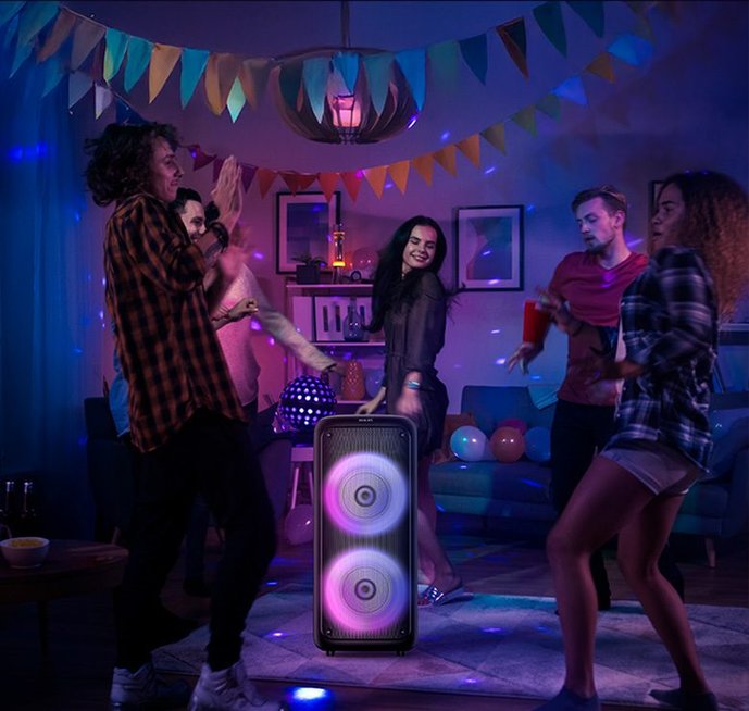 Jovens dançando em sala decorada com luzes e Caixa de Som Philips centralizada no tapete