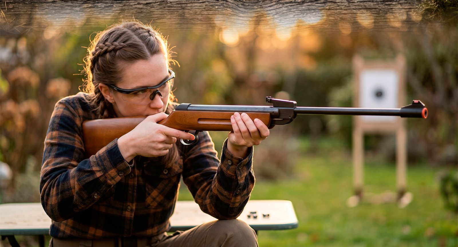 Mulher com óculos de proteção mirando Pistola Airsoft Rossi V17 Green Gas preta em alvos ao ar livre