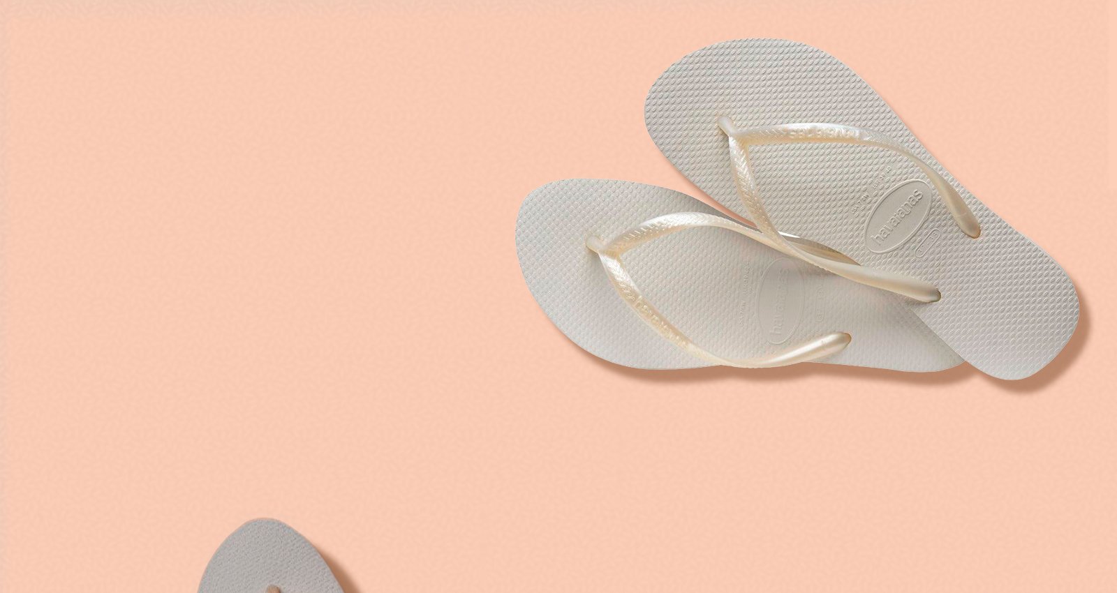 Par de chinelos Havaianas Kids Slim brancos com tiras finas metálicas em fundo pêssego.