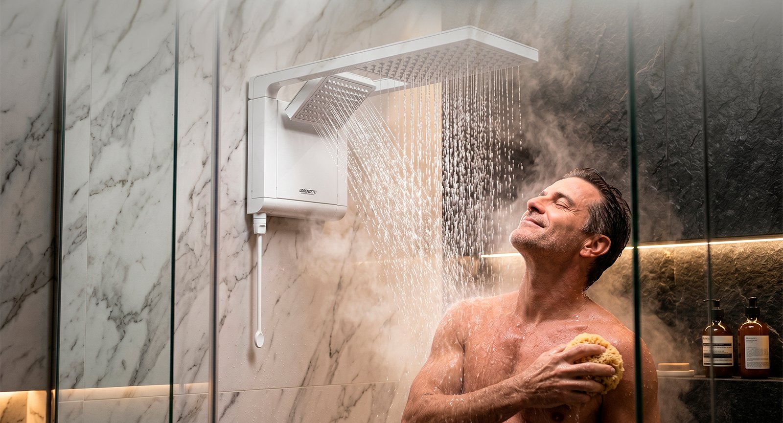 Homem sorrindo em banho com vapor sob queda de água de chuveiro híbrido Lorenzetti Acqua Duo Flex.