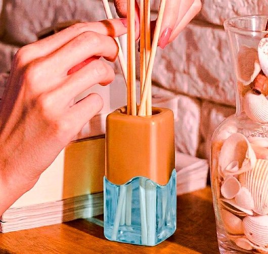 Mão humana ajustando varetas madeira difusor aromas Coala The Queen 100ml vaso conchas fundo