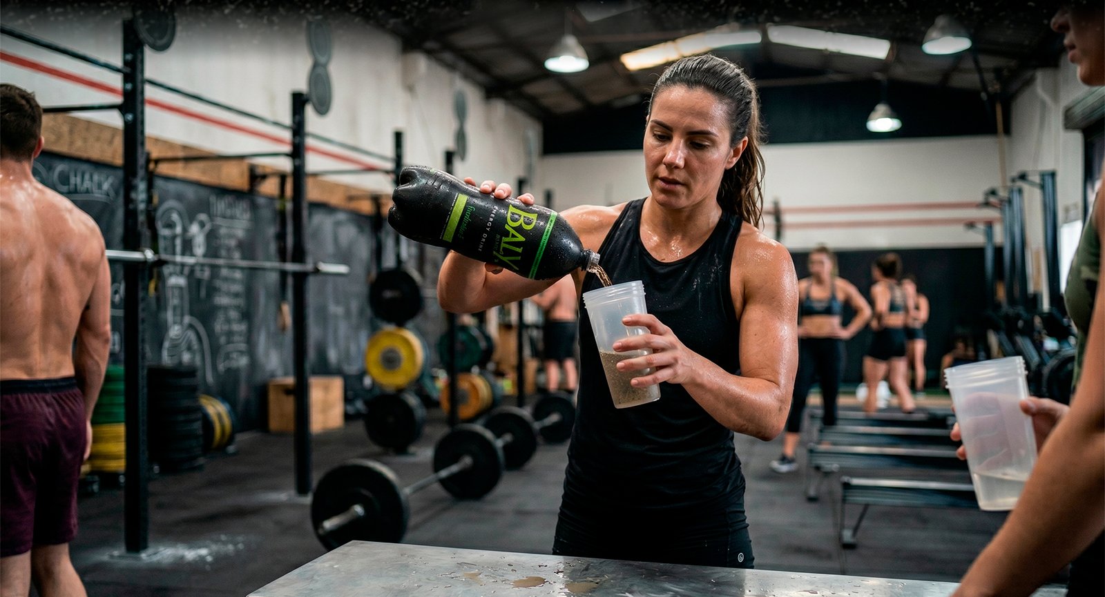 Mulher suada na academia servindo Energético Baly Tradicional Sem Açúcar PET em copo shaker lifestyle