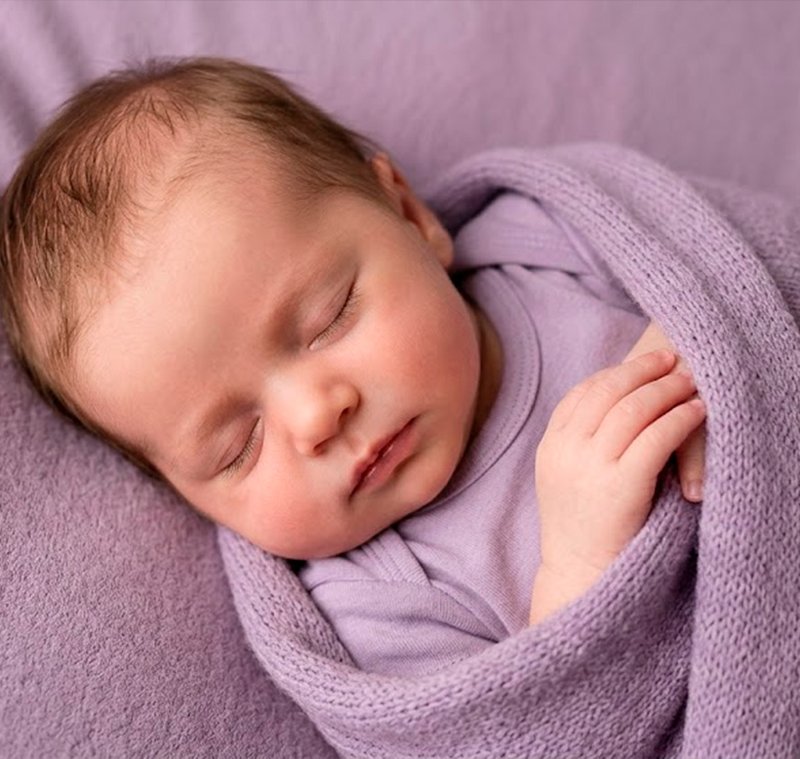 Recém-nascido dormindo tranquilamente enrolado em manta roxa após rotina Johnson's Baby Hora do Sono